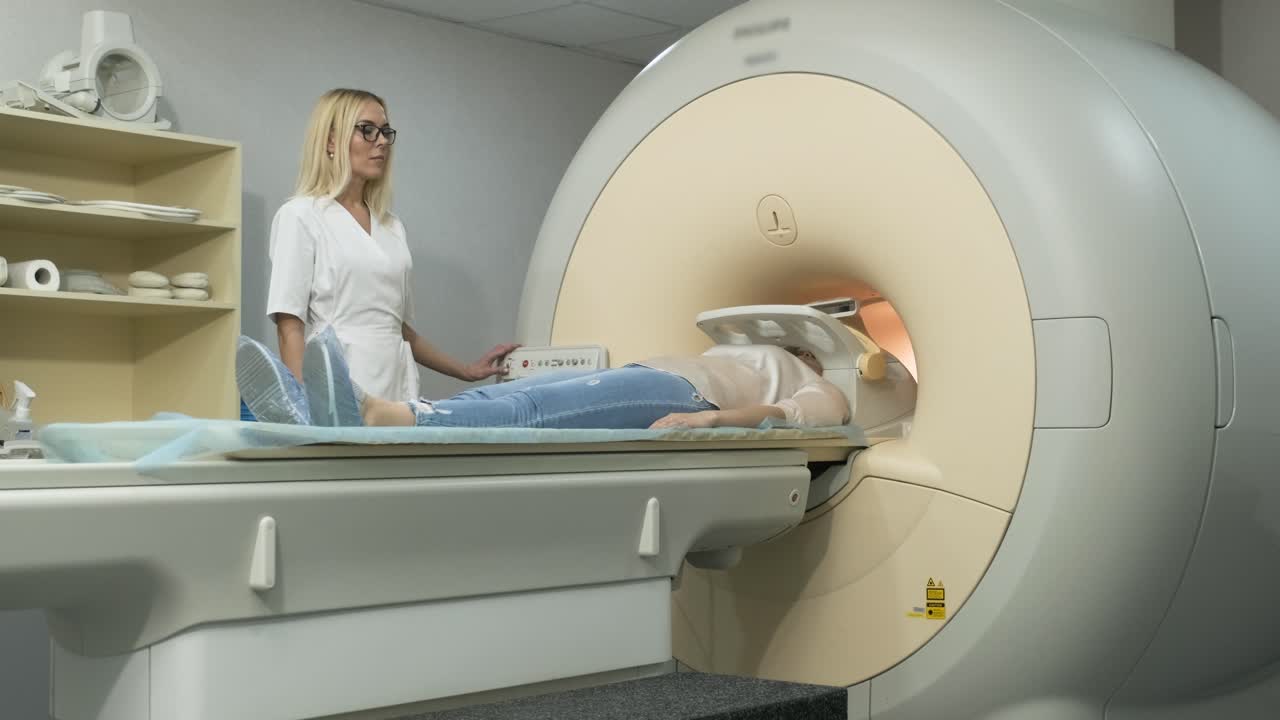 la mujer radióloga hace escaneo de resonancia magnética del cerebro, la cabeza, el cuello. la joven paciente femenina en la mesa automática deja la máquina de mri de tipo cerrado utilizando equipos modernos, bobina en la cabeza del paciente.