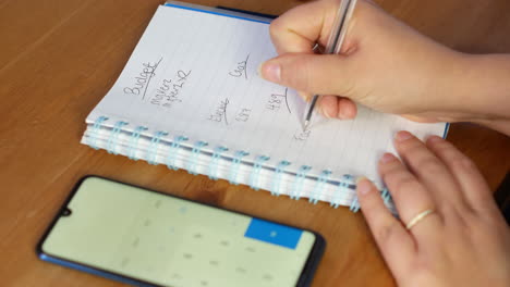 mujer calculando el presupuesto de finanzas familiares en calculadora y escribiendo en cuaderno