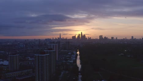 Descending-Aerial-drone-shot-of-London-Canal-Victoria-park-towards-city-skyline-at-sunset