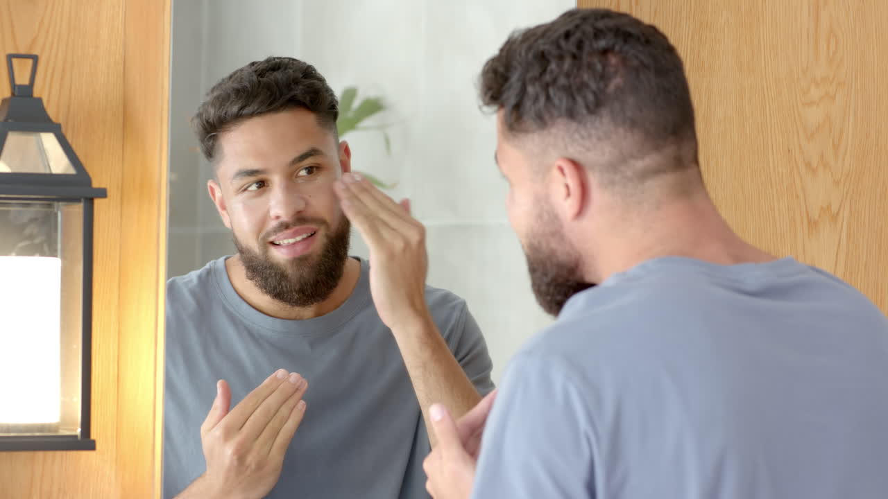Applying skincare product, man looking at reflection in bathroom mirror