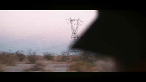 Landscape-and-power-lines-seen-through-window-of-moving-car