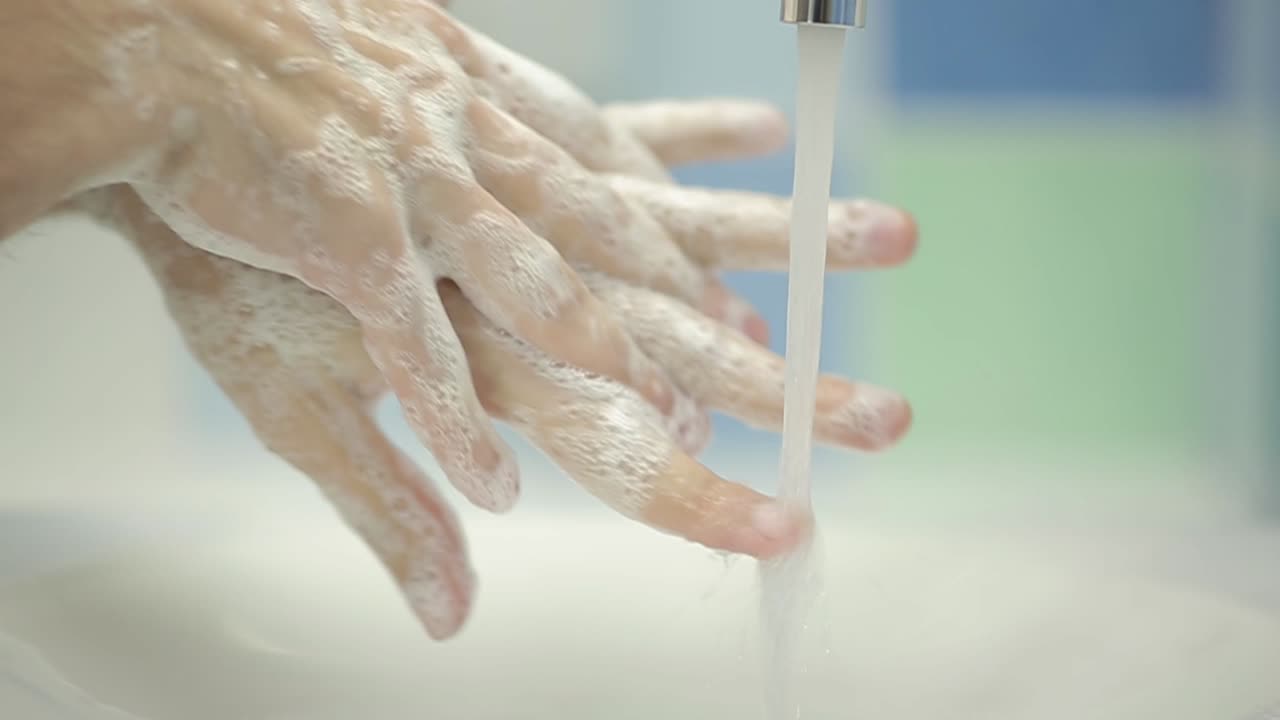 Person, der vasker hænder med sæbe og vand i en håndvask på et badeværelse