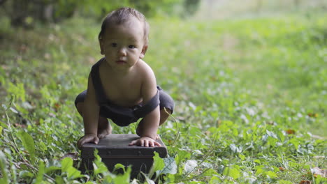 Little-cute-asian-boy-in-the-forest-playing-on-the-grass-barefoot-in-overalls