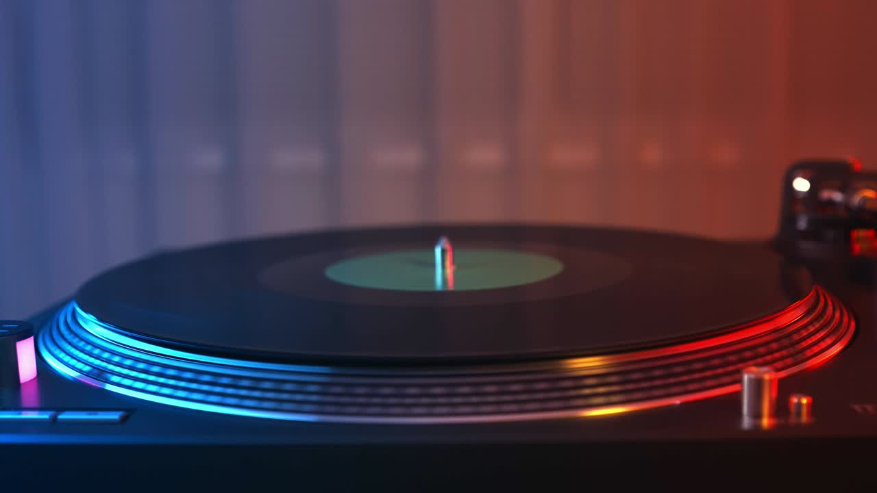 Vinyl record player turntable close-up on a background of red and blue lights. The hand of the young man puts the needle on the rotate plate. DJ at the youth student party