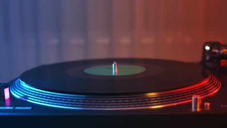 vinyl record player turntable close-up on a background of red and blue lights. the hand of the young man puts the needle on the rotate plate. dj at the youth student party