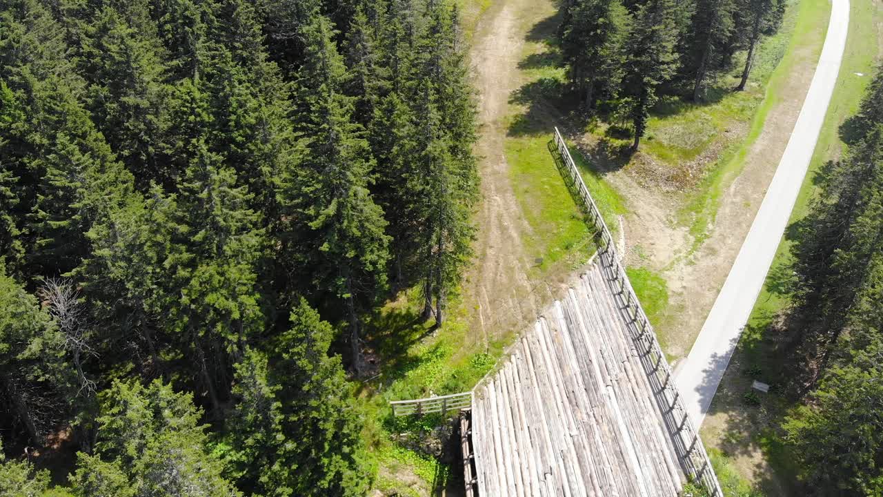 Vehicle bridge at Rogla Slovenia resort forest grounds with walking trail below, Aerial flyover shot