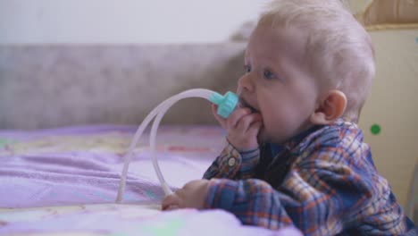little baby in shirt nibbles aspirator at bed in room