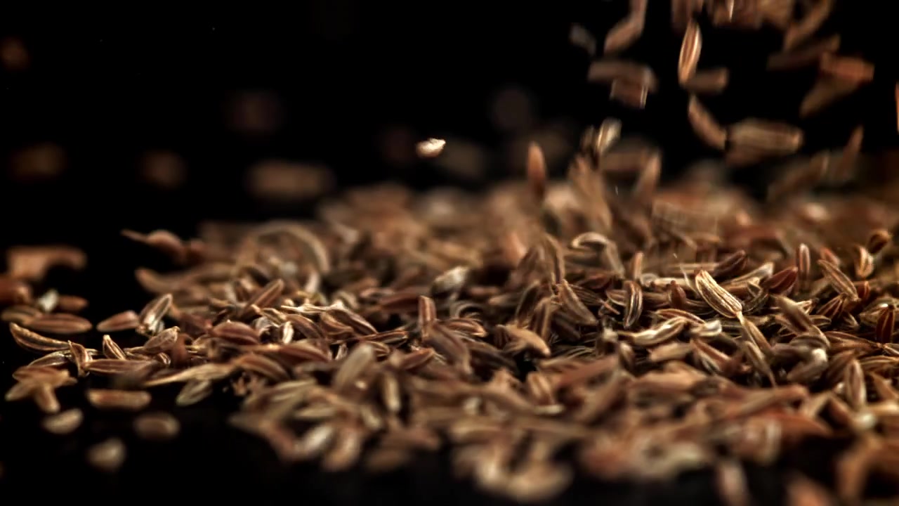 Cumin Seeds Falling and Piling Up on a Black Background