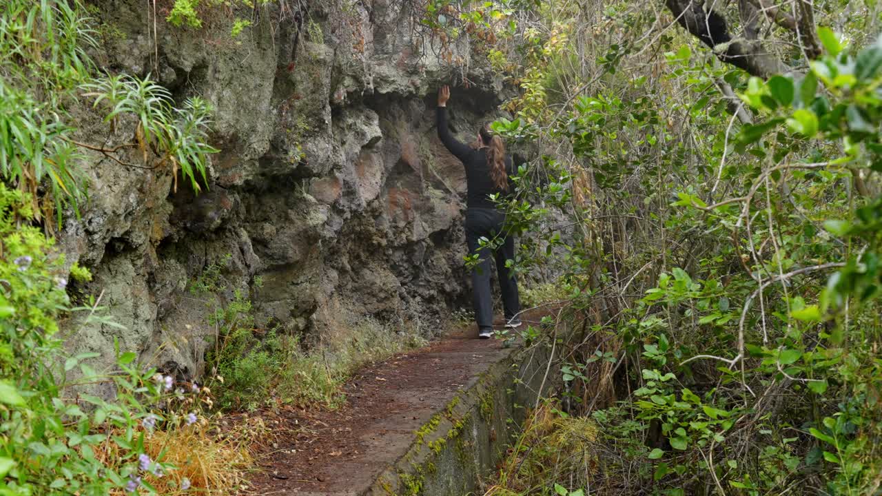 una turista disfruta de caminar a lo largo de un acantilado en tenerife mientras toca las rocas