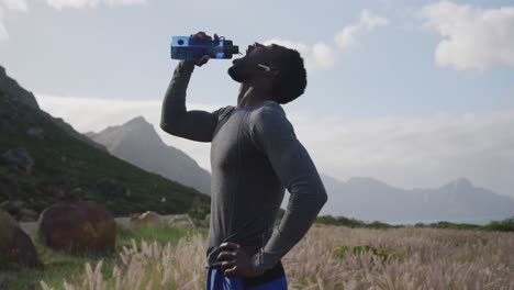 African american man drinking water from bottle while hiking in the mountains