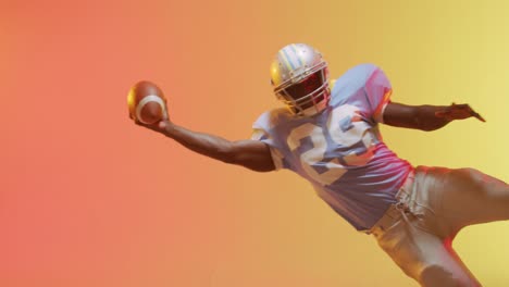 Video-of-african-american-american-football-player-with-ball-over-yellow-to-orange-background