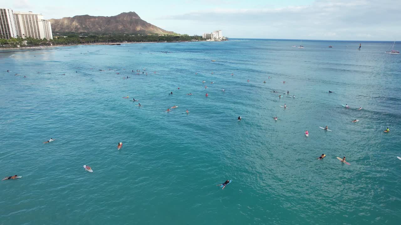 Un drone sorvola in cerchio i surfisti che remano verso il largo per prendere le onde in una località balneare tropicale.