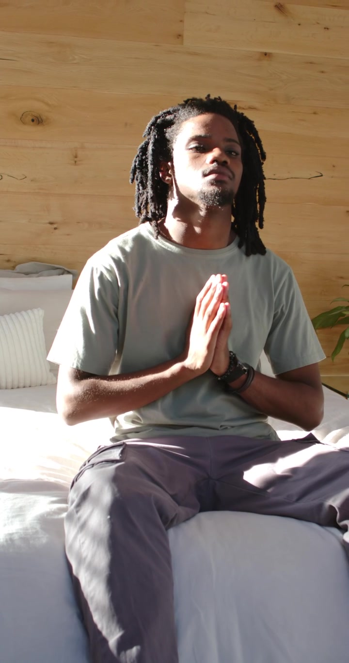 Vertical video: African man praying on bed, meditating as sunlight brightening, opening eyes right