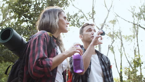 Couple-of-hikers-drinking-fresh-water-and-talking-in-the-forest