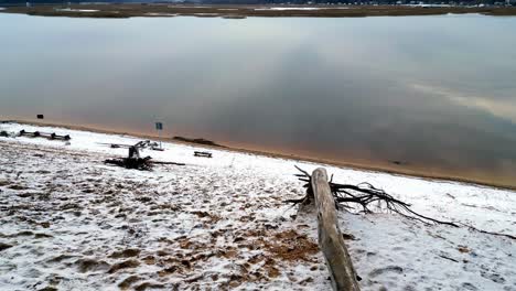 Snowy-coast-of-Lielupe-on-a-beautiful-winter-day,-shore-of-ariver-with-a-line-of-distant-birch-trees-visible-on-the-opposite-bank