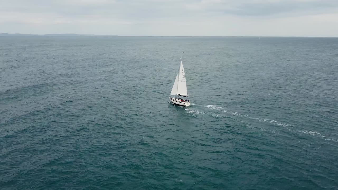 Aerial view of a drone going around a sailing boat, to then expose the English coast far away on the horizon.