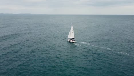 aerial view of a drone going around a sailing boat, to then expose the english coast far away on the horizon.