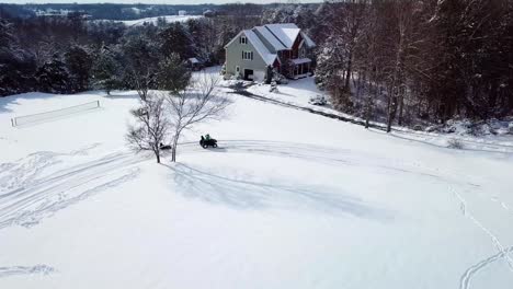 a drone, aerial, birds eye view of an excited child having a fun time playing in the snow by riding a sled which is getting pulled by an atv 4 wheeler with another child riding along and enjoying