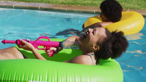 Grupo-Diverso-De-Amigos-Divirtiéndose-Jugando-Con-Pistolas-De-Agua-En-Inflables-En-La-Piscina