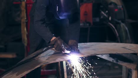 unrecognizable workman all equiped with protective wear cuts piece of mettal with an industrial cutting torch using woodplank to adjust it.