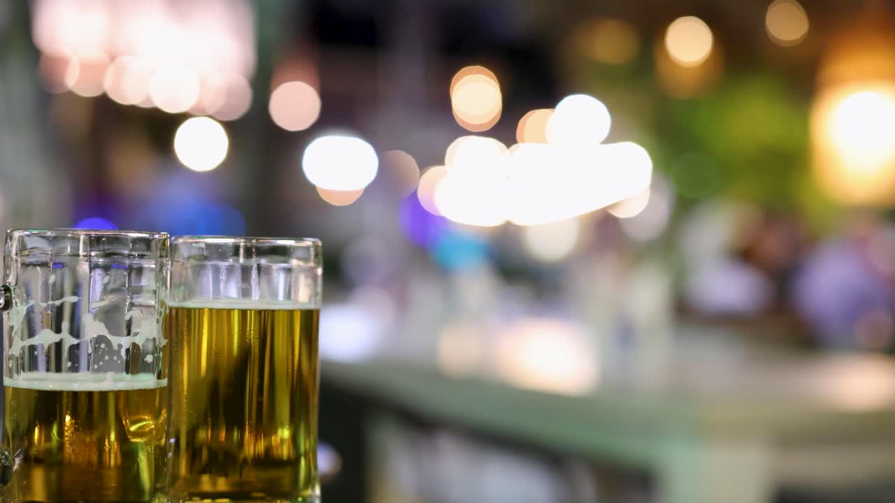 una serie de vasos de cerveza en un mostrador de bar con luces de vida nocturna vibrantes y borrosas en el fondo