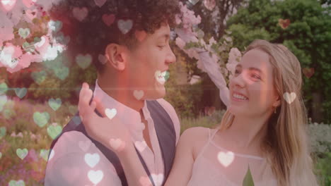 Animación-De-Corazones-Brillantes-Sobre-Una-Feliz-Pareja-Diversa-Sonriendo-En-El-Jardín-El-Día-De-La-Boda