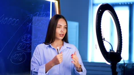 interactive digital lesson. a young woman teaches an online class with a ring light and a chalkboard showing statistics