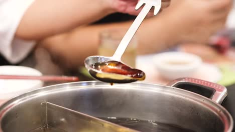 a hand skillfully ladles steaming broth from a hotpot, capturing the essence of a shared meal.
