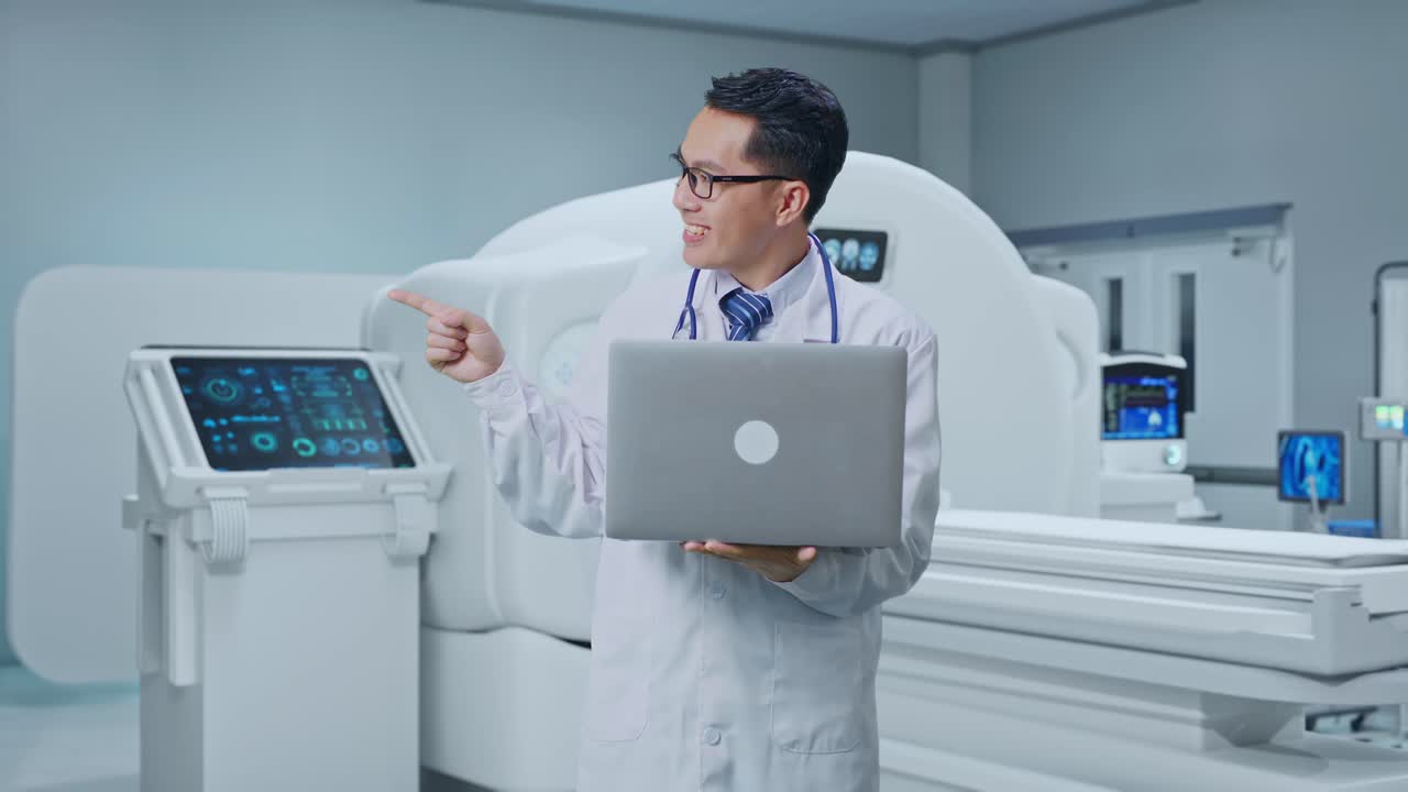 Asian Male Doctor Holding A Laptop, Pointing To The Side And Smiling With MRI Machine In The Hospital