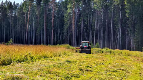 tractor cortando hierba alta en un día soleado con un bosque en el fondo