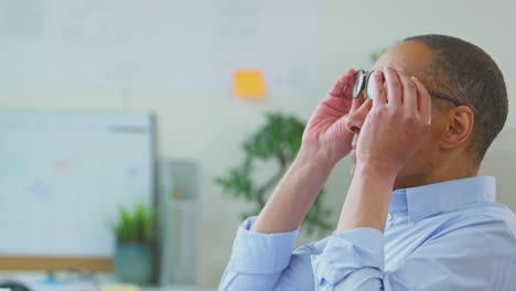 hombre de negocios con gafas en la oficina frotando los ojos mientras trabaja
