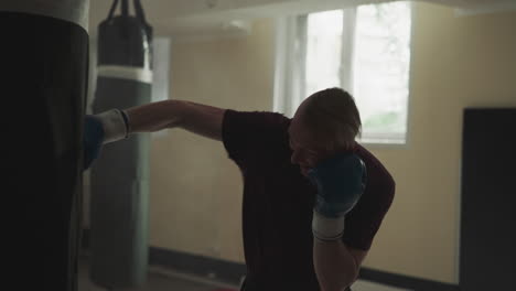 un deportista golpea a una bolsa de boxeo en un club deportivo. un atleta hábil en guantes de boxeo ataca un objeto pesado en un gimnasio de lucha en cámara lenta. un instructor de artes marciales