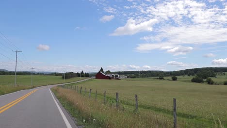 driving down country road with barb wire fences red barn clouds fields power poles