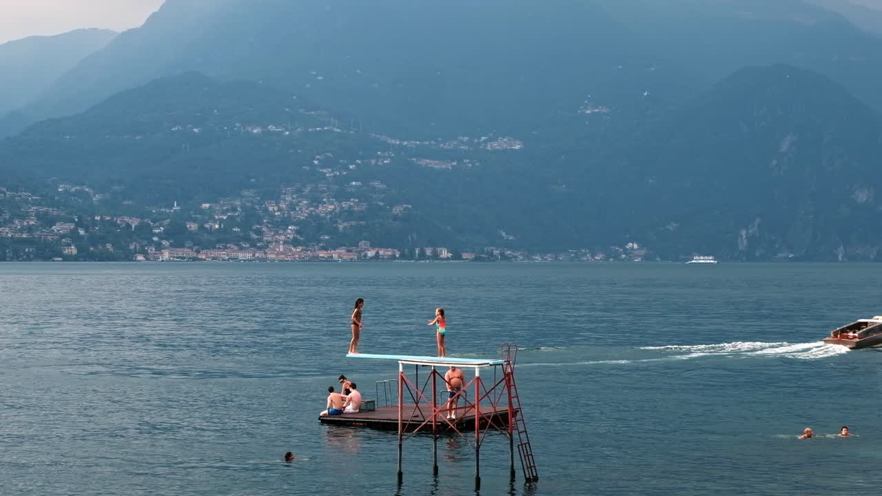 LOMBARDY, ITALY - AUGUST 02, 2018: Cinematic shot of children jumping in lake Como in front of the mountain