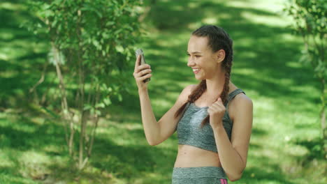 Fröhliche-Läuferin-überprüft-Die-Ergebnisse-In-Der-Mobilen-App-Beim-Joggen-Im-Sommerpark