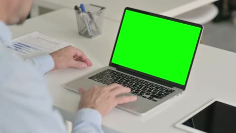 hombre de mediana edad usando una computadora portátil con pantalla de croma verde