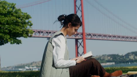 woman reading in a park by a bridge