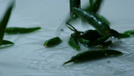 Whole-Green-Hot-Peppers-Fall-into-Water-on-White-Background-in-Slow-Motion