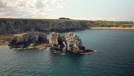 long arc aerial around massive rocky cliff adjacent to body of water