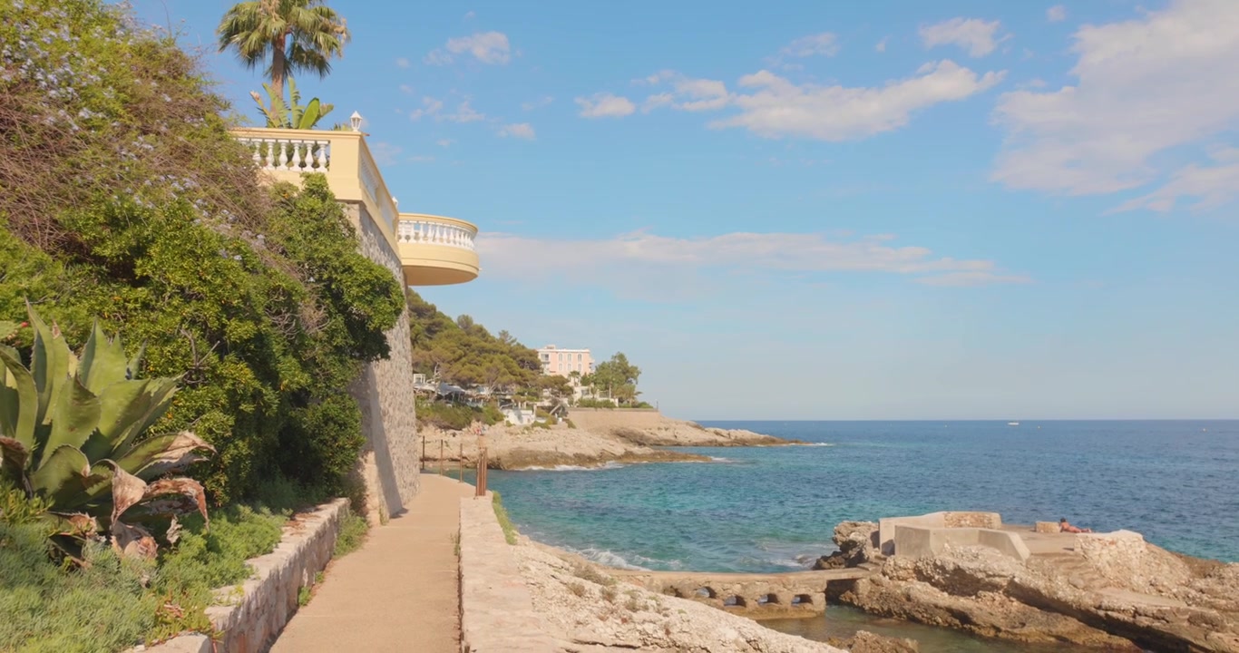 Sentiero costiero soleggiato con vegetazione lussureggiante e vista mare a Cap d'Ail, Costa Azzurra.
