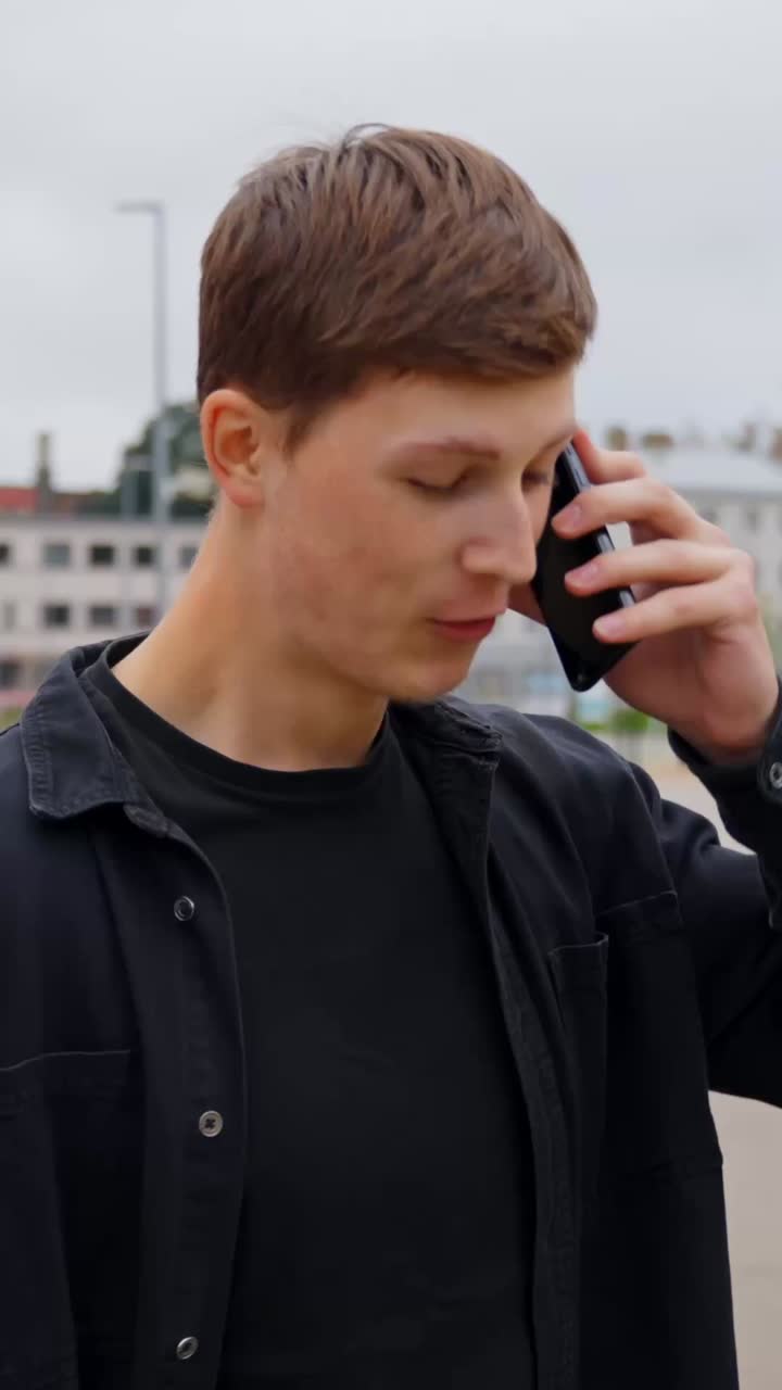 Vertical shot of a young man talking on a mobile phone in a city, communication