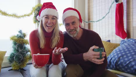 Happy-caucasian-mature-couple-making-video-call-in-room-full-of-christmas-decorations