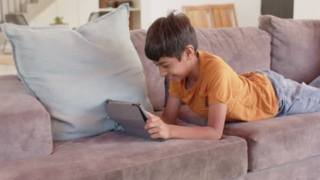 lying on couch, boy using tablet and smiling, enjoying leisure time at home