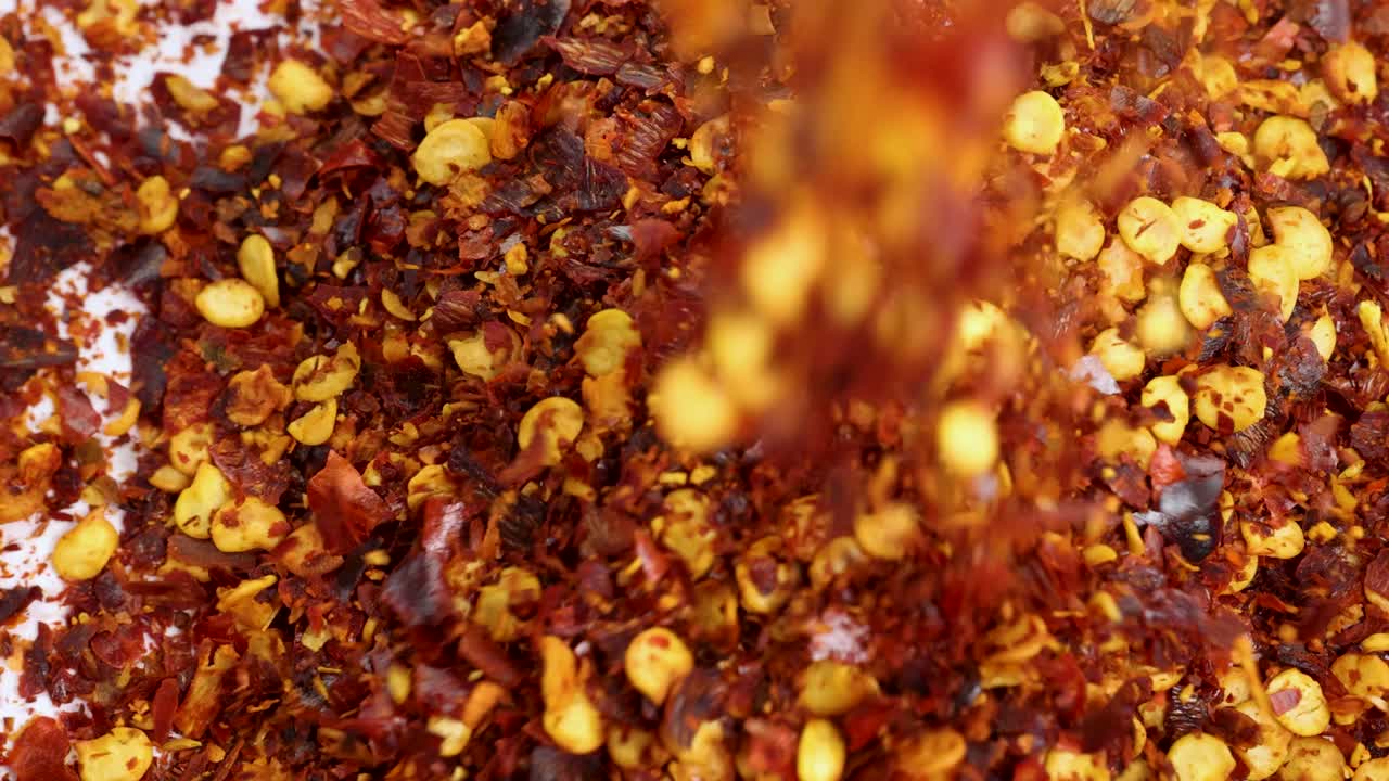 Dried chili flakes cascade onto a white surface in a vibrant, close-up macro shot with dynamic motion