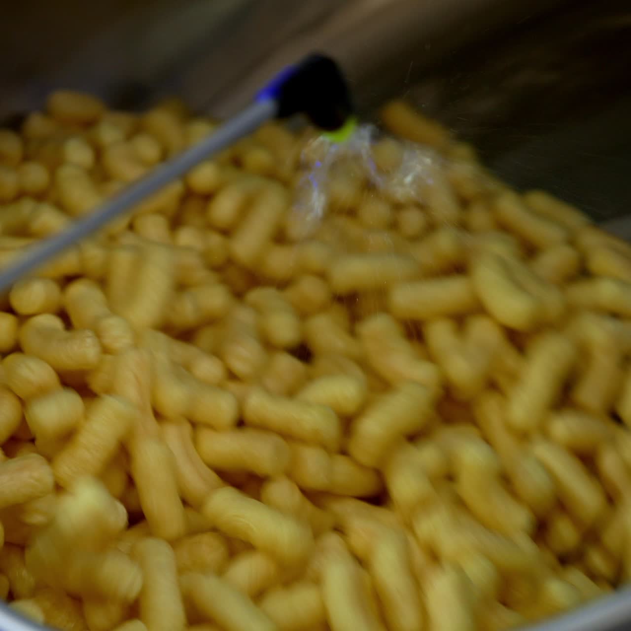 Delicious crispy snacks covered with liquid sweet syrup. Maize sticks spinning in the metal tank at food factory. Close up