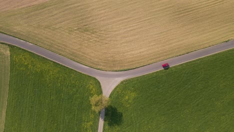 red car travelling along an open country road through rural farmland