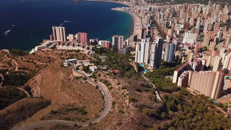 Luftaufnahme-Von-Hohen-Wohn--Und-Geschäftsgebäuden-In-Der-Nähe-Des-Strandes-Mit-Blick-Auf-Das-Stille-Meer,-Umgeben-Von-Bergen-In-Der-Stadt-Benidorm-In-Spanien