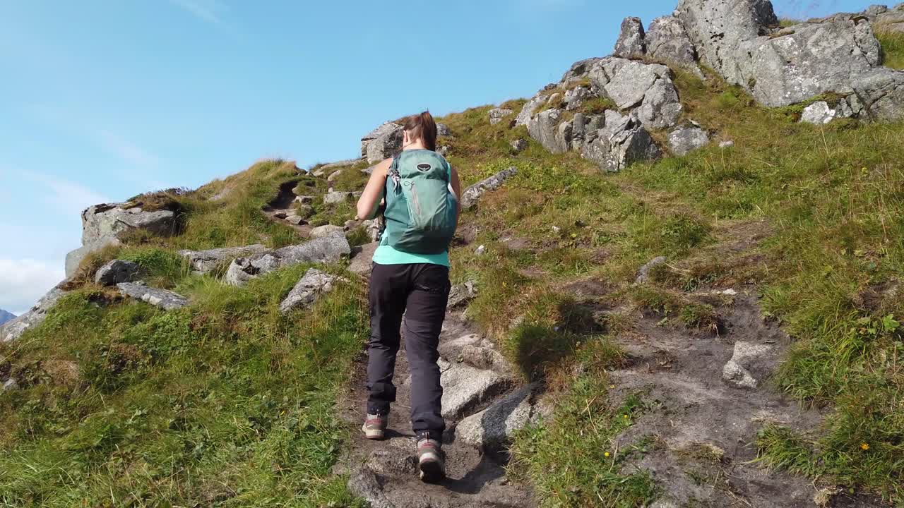 una joven morena camina con sus botas de montaña y su mochila por un sendero que conduce a la cima de la montaña mannen