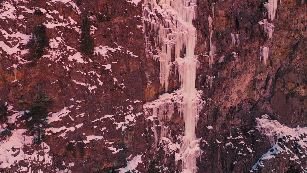 levantándose a lo largo de una gran línea de hielo en un acantilado rocoso nevado al amanecer para revelar el lago del bosque y la isla detrás