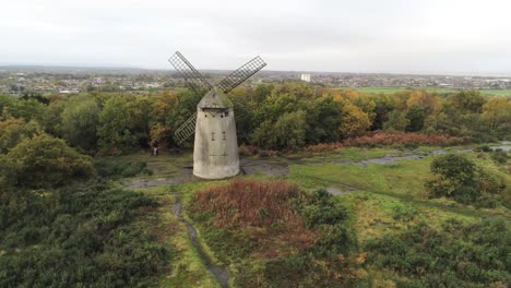 Traditionelle-Holzmühle-Windmühle-Aus-Stein-Erhalten-Im-Herbst-Wald-Luftbild-Landschaft-Wegziehen-Orbit-Rechts